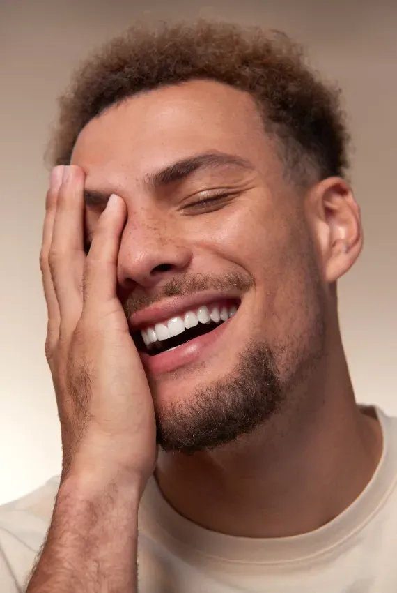 Hombre joven con una mano tocándose la cara, sonriendo.